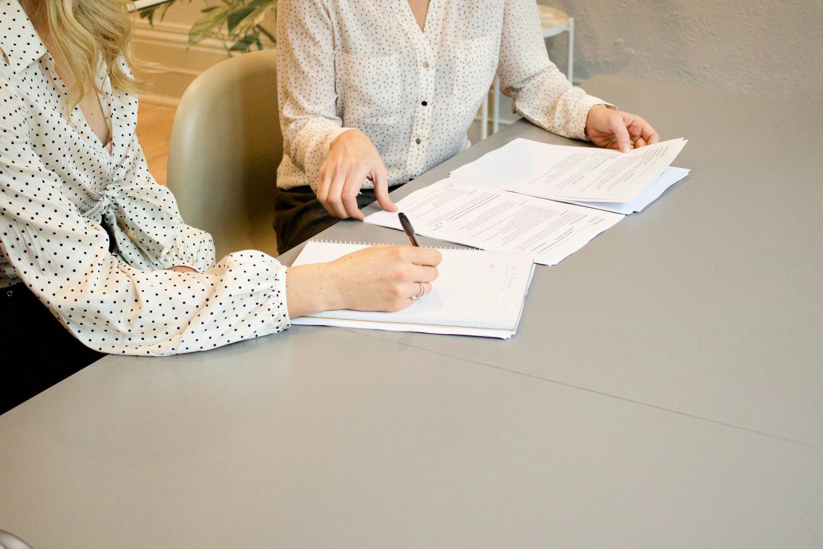 Photo by Gabrielle Henderson woman signing on white printer paper beside woman about to touch the documents